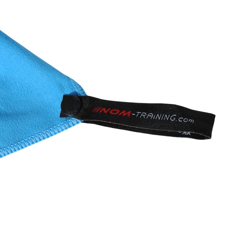 "Detailaufnahme eines blauen NOM Training Handtuchs mit schwarzem Befestigungsband und NOM-Training.com-Logo."